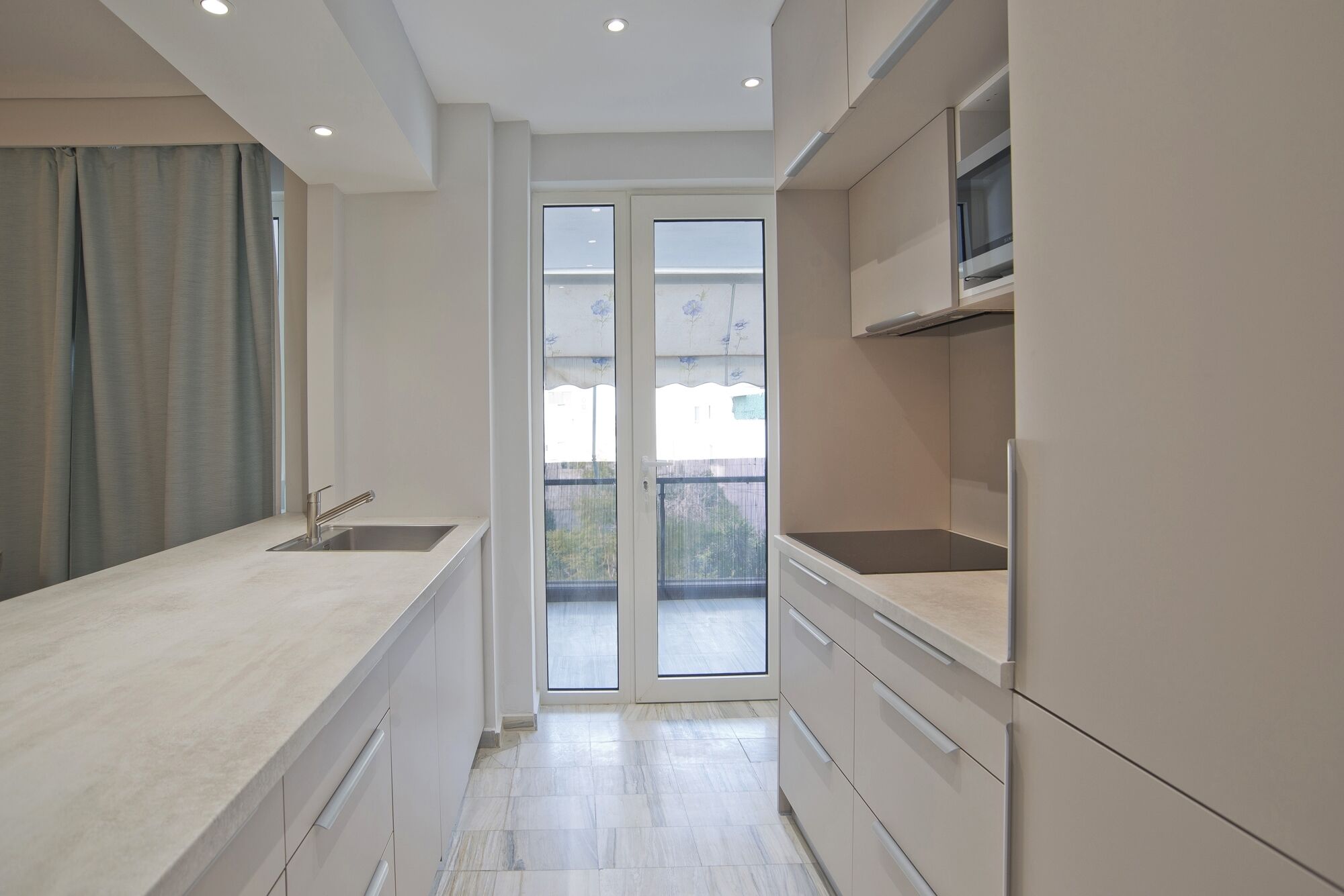 A narrow kitchen with a sink, cabinets, and a view through a glass door to an outdoor balcony.