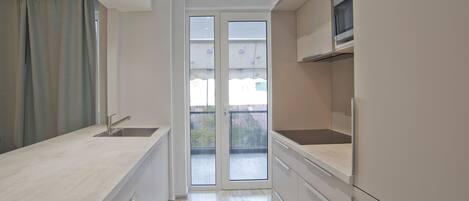 A narrow kitchen with a sink, cabinets, and a view through a glass door to an outdoor balcony.