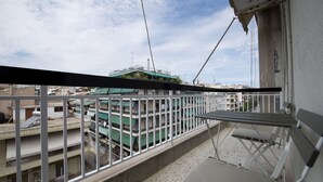 A balcony with a metal railing, a folding chair, and a view of a building with multiple floors and a green roof. - Alemar Quiet Kallithea Retreat with AC, Wifi (Kalithea)