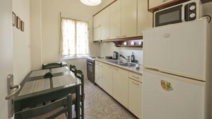 A compact kitchen with a dining table, chairs, a refrigerator, a microwave, and a window with curtains. - Alemar Quiet Kallithea Retreat with AC, Wifi (Kalithea)