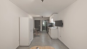 Une cuisine moderne équipée d’un téléviseur à écran plat, d’un coin repas avec une table ronde et des chaises, et d’un couloir menant à une porte.