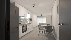 Une cuisine moderne avec des meubles blancs, un four encastré et un coin repas comprenant une table et des chaises.