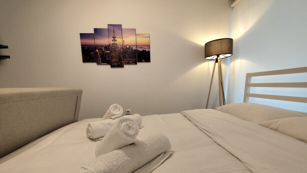 Une chambre d’hôtel avec un lit parfaitement fait, une œuvre d’art représentant un paysage urbain accrochée au mur et une lampe sur pied.