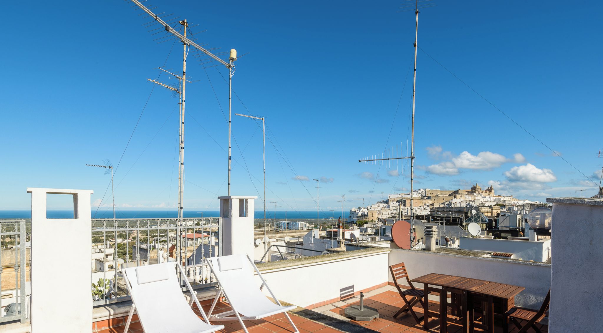 Una terraza en la azotea con sillones blancos, una mesa de madera y vistas a un pueblo costero.