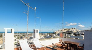 Une terrasse sur le toit, avec des chaises longues blanches, une table en bois et une vue sur une ville côtière.