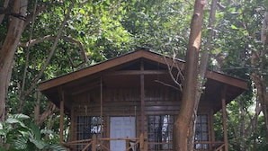 Een houten hut met een veranda, omgeven door dicht bos.