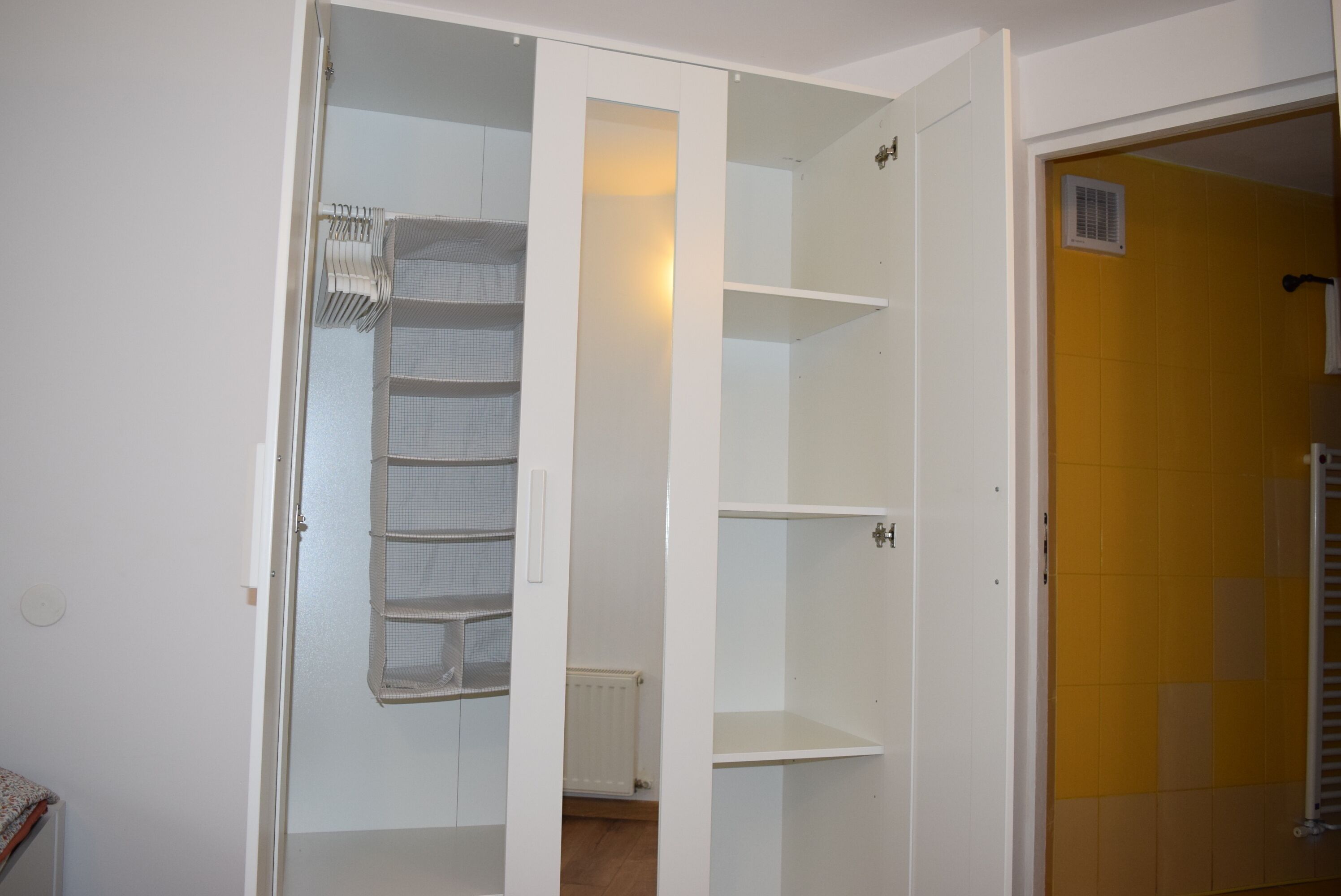 Habitació amb un armari blanc, una paret groga i un radiador.