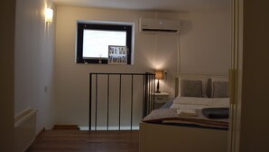 Ein Schlafzimmer mit Bett, Fenster mit Jalousien, Klimaanlage und Nachttisch mit Lampe.