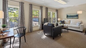 A well-lit living room with a sofa, a dining table with chairs, and a TV.