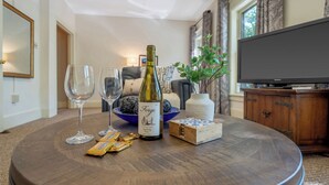A round wooden table with a wine bottle, two wine glasses, a bowl of chocolates, and a small wooden box.