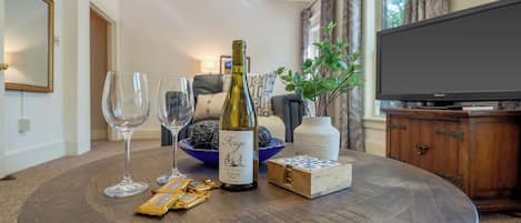 Uma mesa de madeira redonda com uma garrafa de vinho, duas taças de vinho, uma tigela de chocolates e uma pequena caixa de madeira.