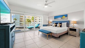 Une chambre spacieuse avec un grand lit, un ventilateur de plafond, une télévision et un balcon avec vue sur la piscine.