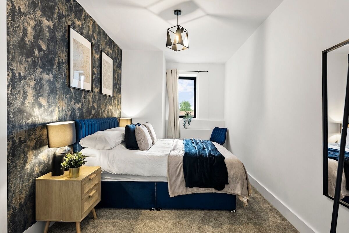 Une chambre moderne avec un lit, des tables de chevet, une commode, un luminaire suspendu et une fenêtre donnant sur un beau paysage.