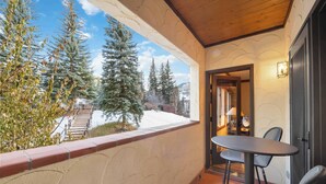 A balcony with a view of snow-covered mountains and trees. There is a table and two chairs. - The Charter at Beaver Creek E1505 (Beaver Creek)