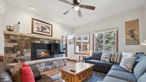 A cozy living room with a stone fireplace, leather sofas, and a large window offering a view of the outdoors. - The Charter at Beaver Creek E1505 (Beaver Creek)