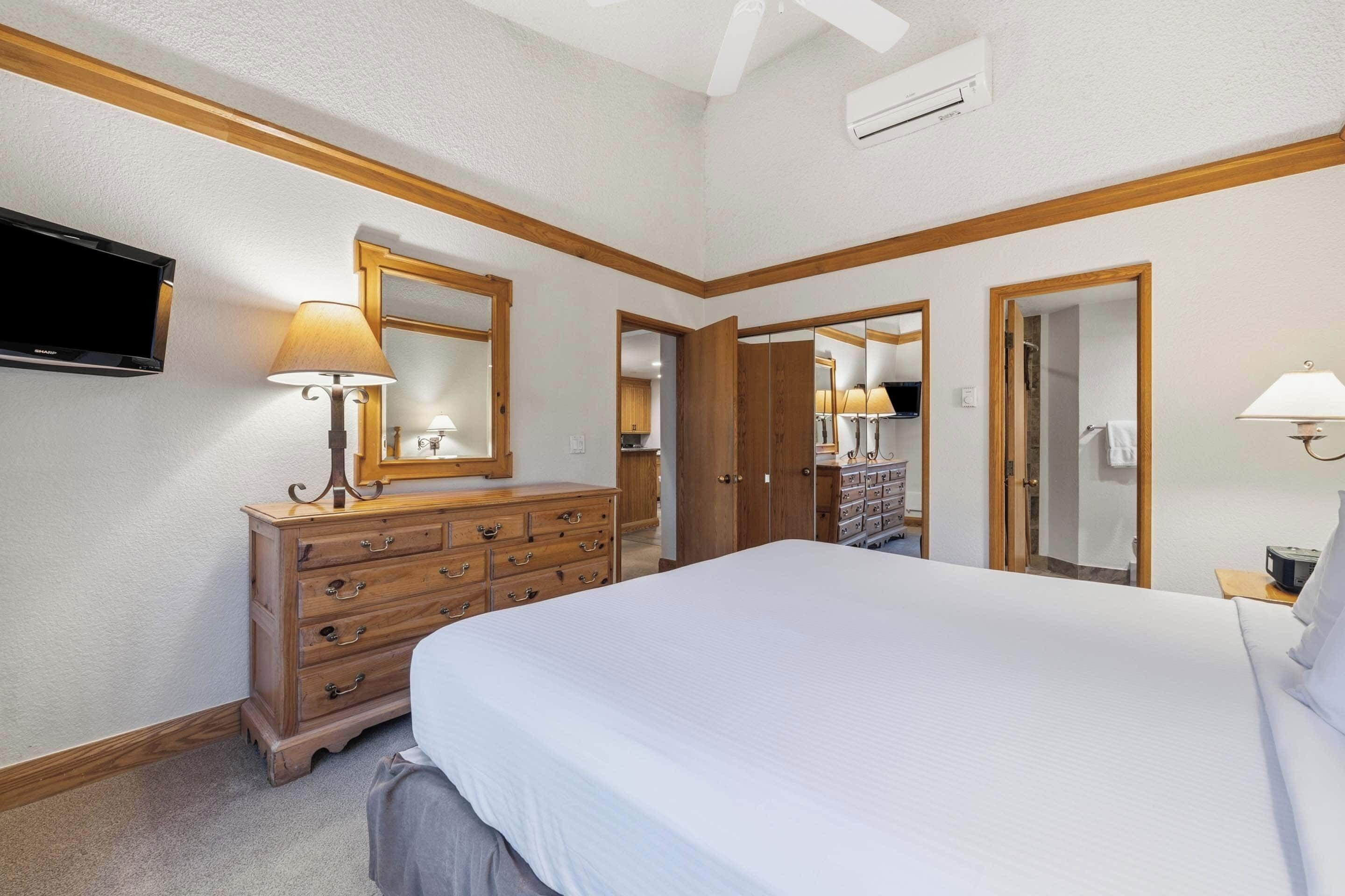 Una camera d'albergo con un letto grande, una cassettiera in legno e un televisore fissato alla parete.