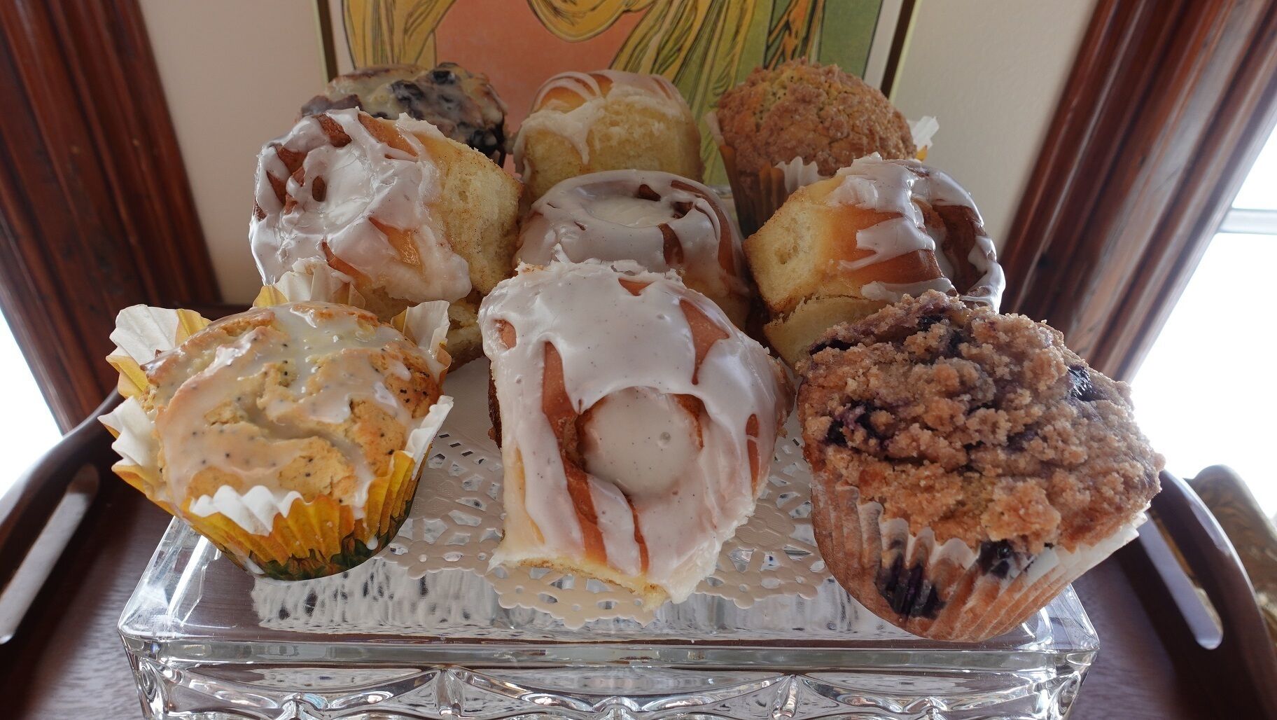 A tray of assorted muffins with white icing, placed on a glass serving tray.