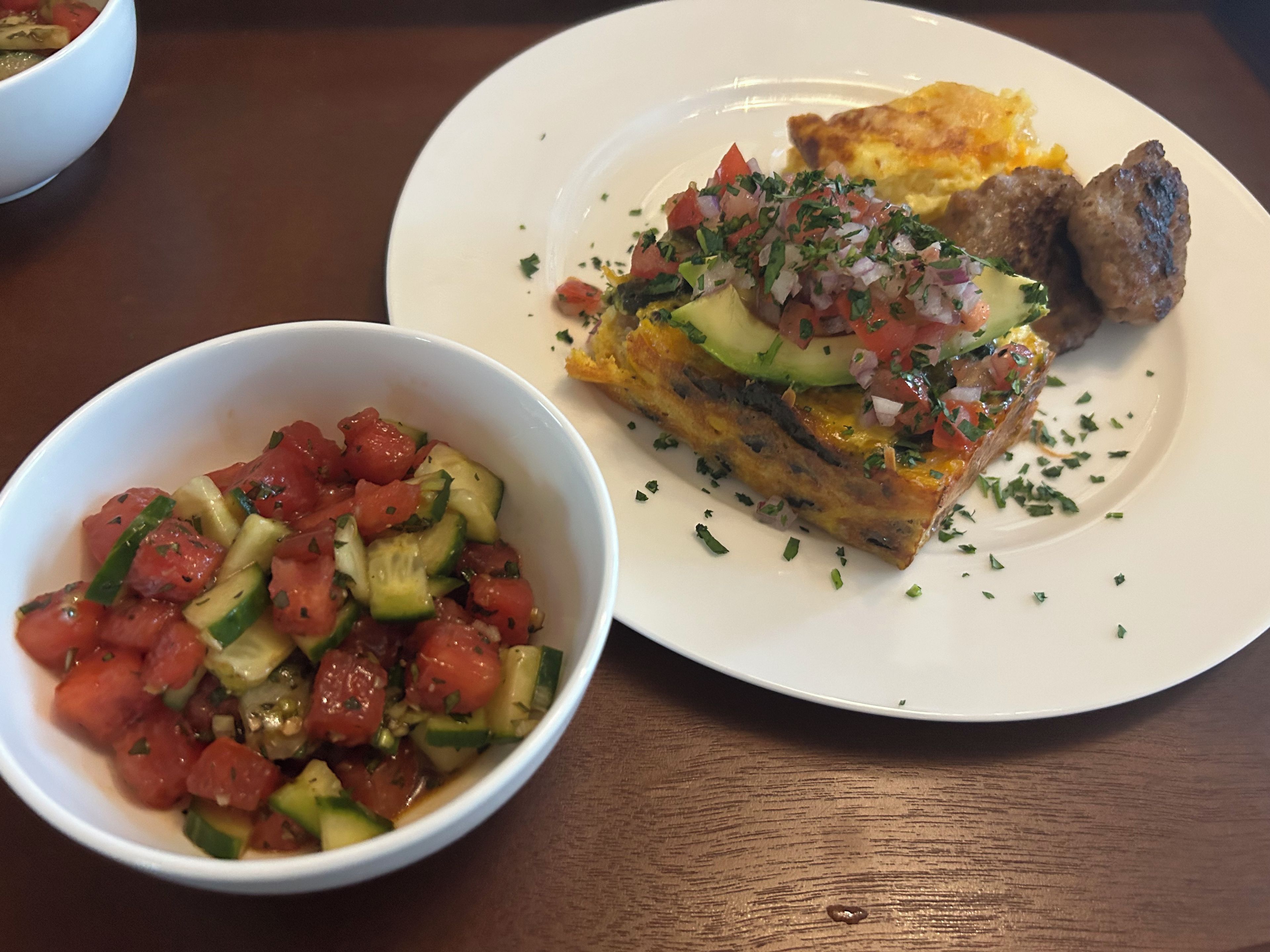 A plate with a slice of pizza topped with vegetables and meat, a bowl of vegetable salad, and a white plate with a piece of toast.