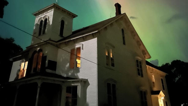 A white building with a tower and multiple windows, under a night sky with a visible aurora. - Hancock Historic Bed & Breakfast with Personal Chef Made-to-Order Full Breakfast (Hancock)