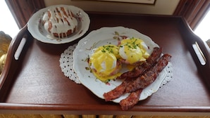 A tray with two plates of eggs benedict and bacon, and a single pastry on a doily. - Hancock Historic Bed & Breakfast with Personal Chef Made-to-Order Full Breakfast (Hancock)