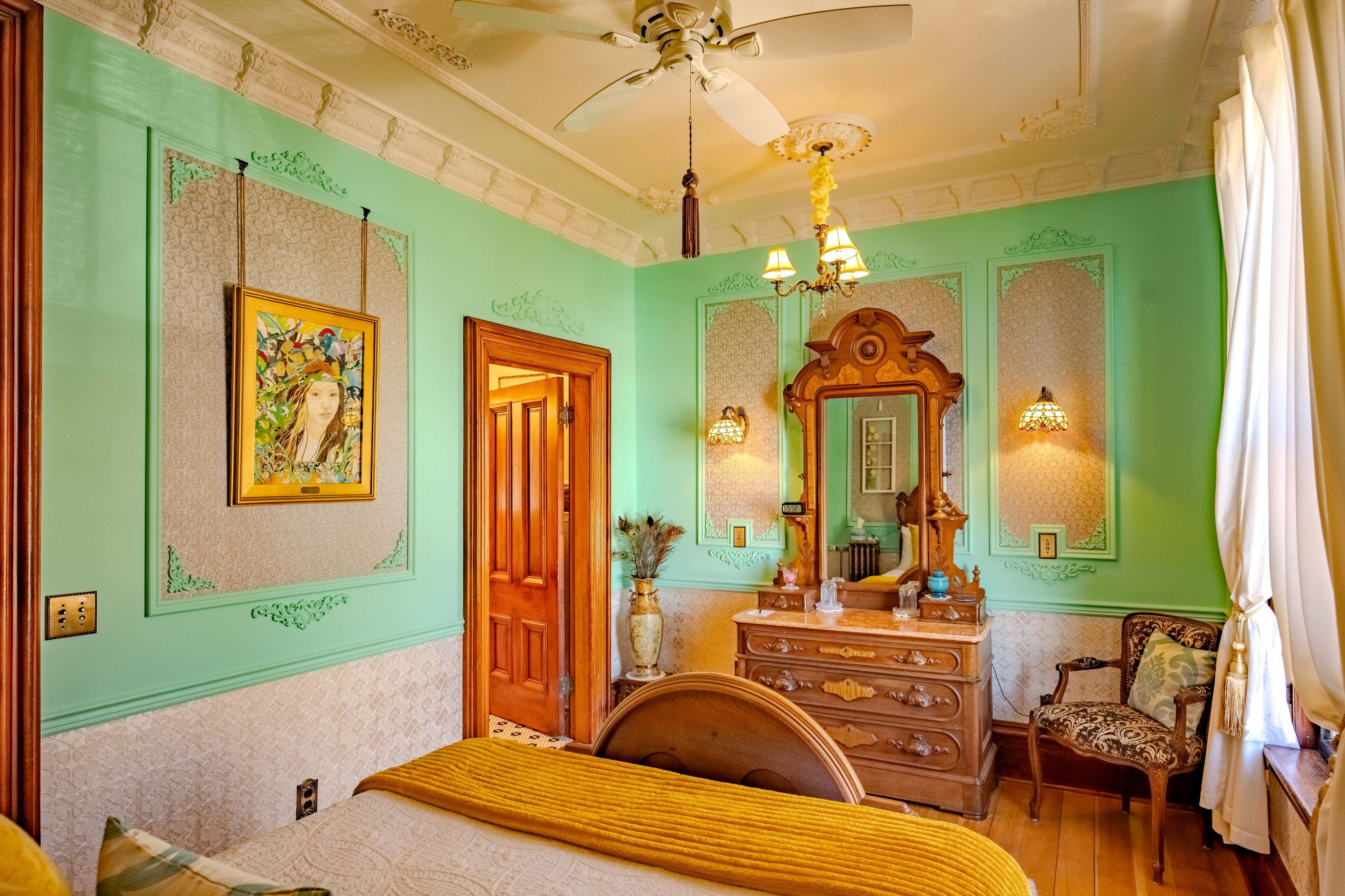 A room with a bed, a dresser, a chair, a ceiling fan, and a mirror.