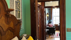 A room with a wooden bed, a green wall, and a door leading to another room with a lamp and a chair. - Hancock Historic Bed & Breakfast with Personal Chef Made-to-Order Full Breakfast (Hancock)