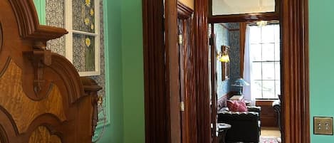 Una habitación con una cama de madera, una pared verde y una puerta que da a otra habitación con una lámpara y una silla.