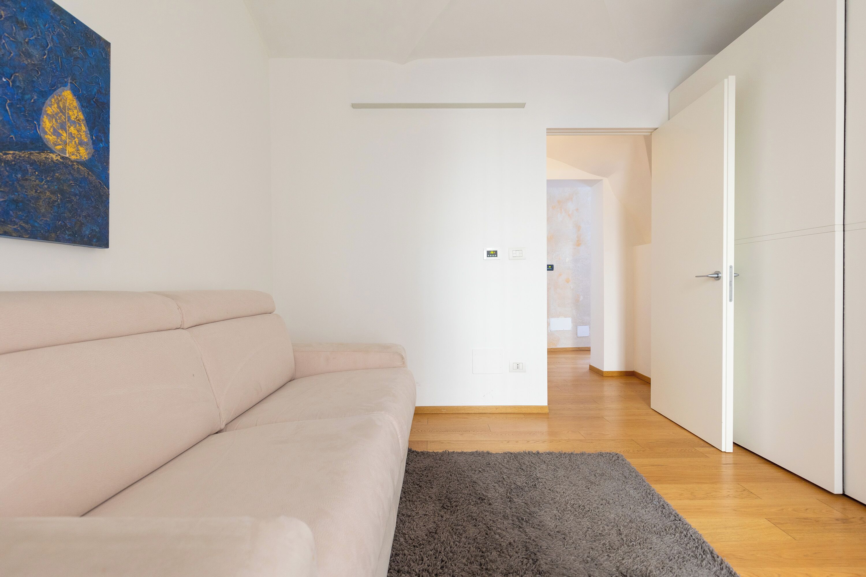 Un salón moderno con un sofá beige, un tapete gris y un cuadro azul en la pared.