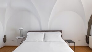 A bedroom with a bed, a bedside table, a lamp, and a stone wall.
