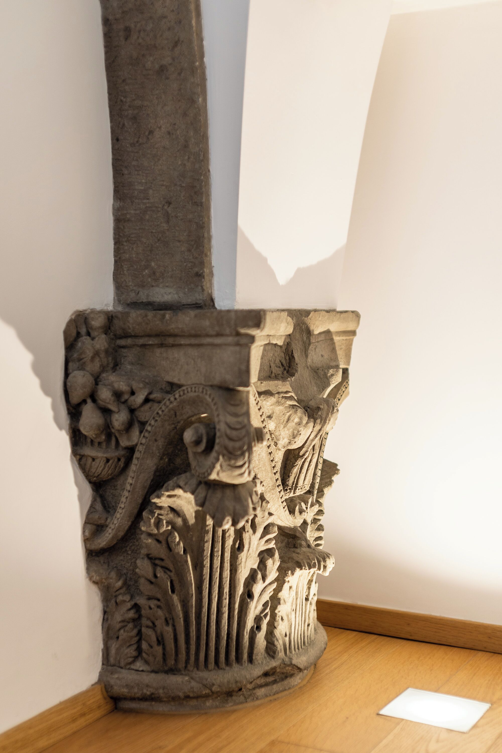 A stone column with intricate carvings, including floral and foliage motifs, positioned against a plain wall.