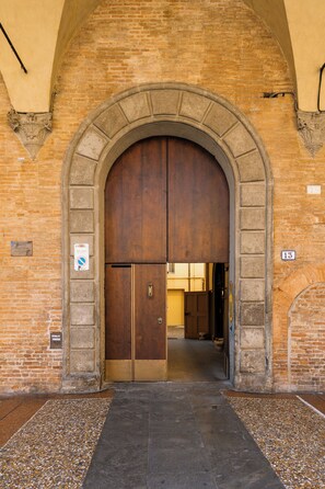 Una entrada arqueada con una puerta de madera, un muro de ladrillo y un suelo de baldosas.