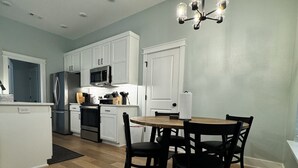 Une cuisine moderne avec des meubles blancs, un réfrigérateur en acier inoxydable, un four à micro-ondes et un coin repas comprenant une table en bois et quatre chaises.