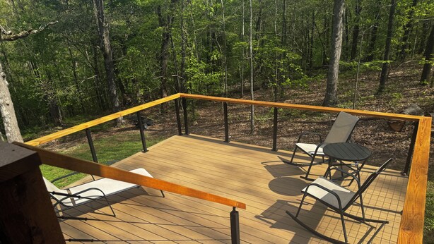 Une terrasse en bois, agrémentée de mobilier d’extérieur, entourée d’une rambarde et offrant une vue sur une zone boisée.