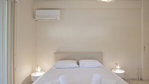 A hotel room with a bed, two bedside tables with lamps, an air conditioning unit, and a ceiling light fixture. - Riviera Living in Vouliagmeni (Vari-Voula-Vouliagmeni)
