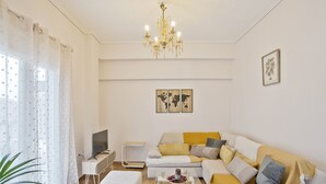 Een moderne woonkamer met een bank, een glazen salontafel, een televisie en een kroonluchter.