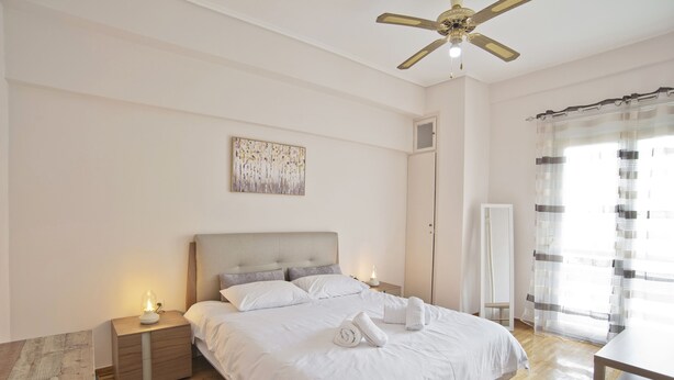 Een slaapkamer met een bed, nachtkastjes, een plafondventilator, een schilderij en een raam met gordijnen.