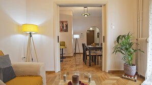 Een woonkamer met een bank, een bijzettafeltje met decoratieve spullen, een lamp, en een eethoek op de achtergrond.