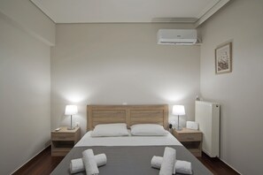 Habitación de hotel ordenada con una cama grande, dos mesitas de noche con lámparas, un radiador y un cuadro en la pared.