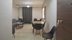 Ein modernes Wohnzimmer mit einer Couch, einem Couchtisch, einem Esstisch mit Stühlen und einem großen Fenster.