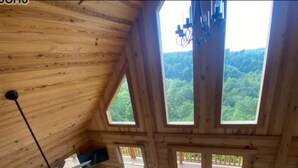 A wooden cabin interior with a sofa, a ceiling fan, and large windows offering a forest view. - Dale Hollow Lakeview Getaway Log Cabin•3 Bedroom•2.5 Baths•Scenic View•Game Room (Byrdstown)
