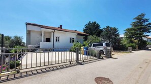 A single-story house with a tiled roof, a gated driveway, and a parked white vehicle.