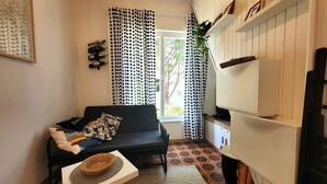 Ein kompakter Wohnraum mit einer Couch, einem kleinen Tisch, einem Fernseher und einem Fenster mit Vorhängen.