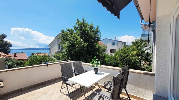 Ein Balkon mit Tisch und Stühlen, einem Blumentopf und Blick auf das Meer und Gebäude.