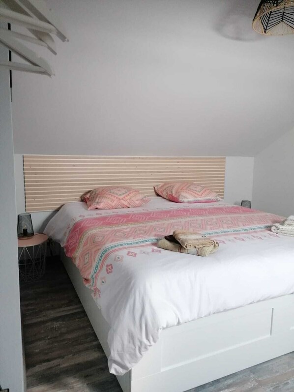 Een slaapkamer met een wit bed, kussens met een roze patroon en een houten hoofdbord.