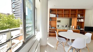 Un soggiorno moderno con una grande finestra, un'area pranzo con sedie bianche, un tavolo in vetro e una libreria in legno.