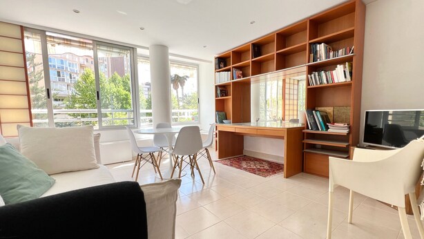 Un soggiorno moderno con una grande finestra, una libreria in legno, un'area pranzo e una televisione.