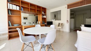 Un soggiorno moderno con un tavolo da pranzo rotondo, sedie bianche, una libreria, un televisore piatto e un grande specchio.
