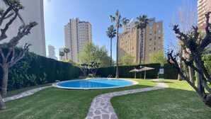 Una piscina circondata da un vialetto in pietra, un prato verde e rigoglioso e alti edifici sullo sfondo.