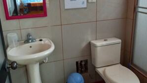 Een badkamer met een wastafel, toilet en spiegel. Er hangt een bord aan de muur en er staat een prullenbak.