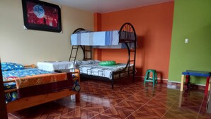 A dormitory room with two bunk beds, a small table, and a green stool.
